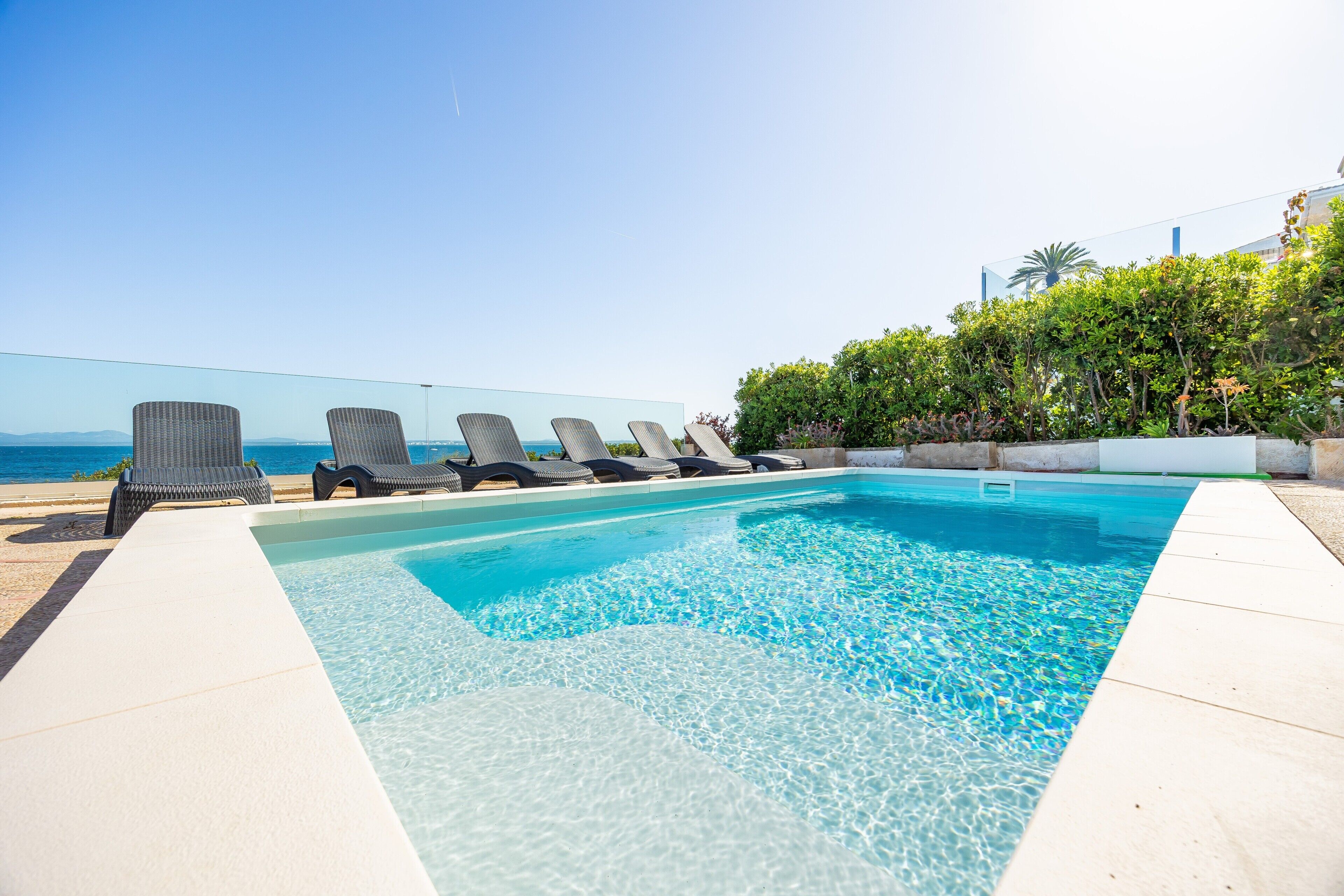 Ein Pool mit klarem Wasser, umgeben von Liegestühlen und Blick auf den Ozean.