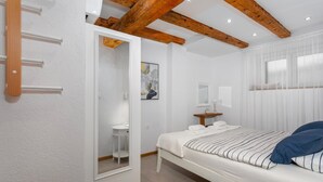 A bedroom with a bed, a bedside table, a mirror, and a window with curtains.