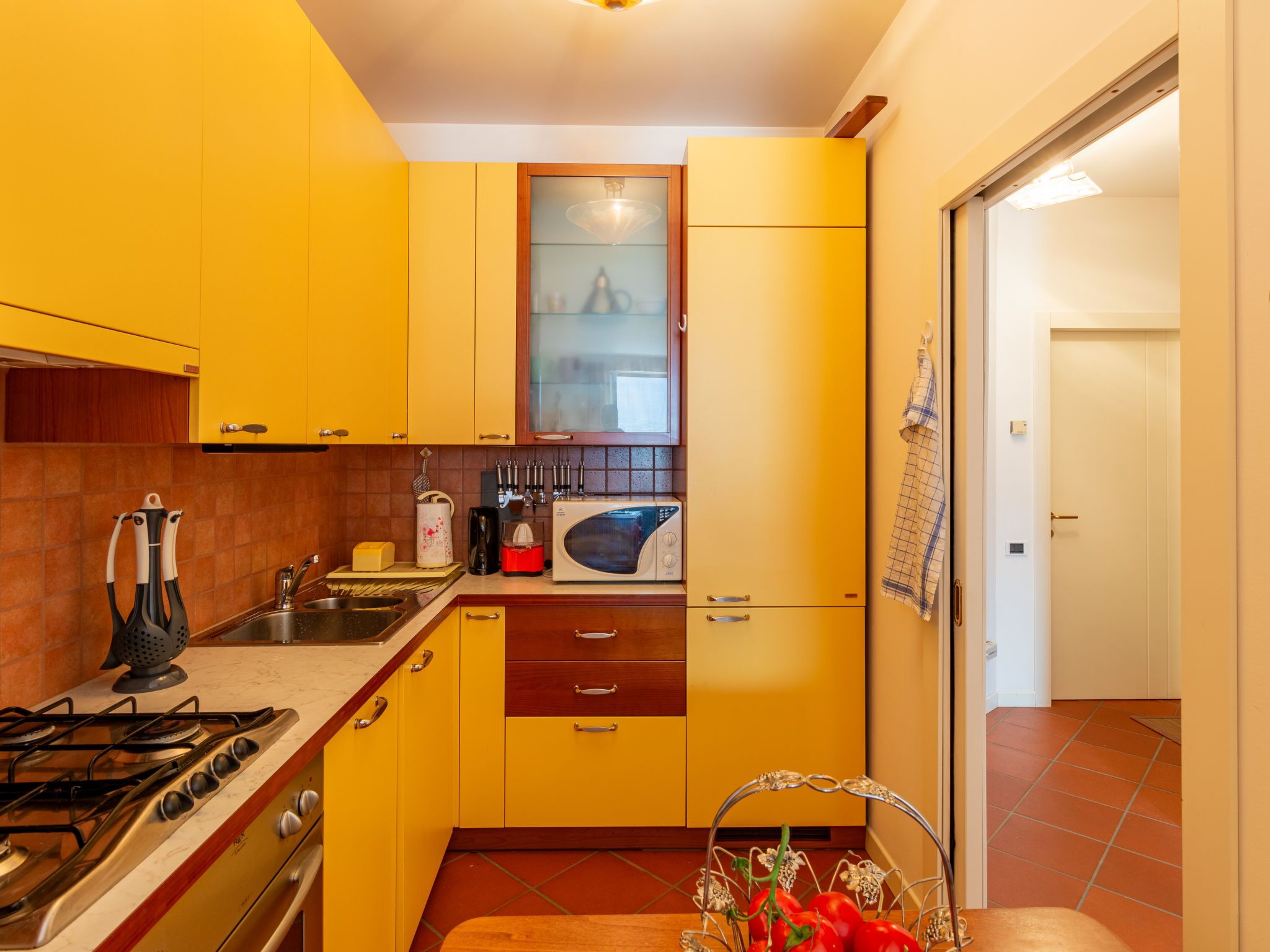 A compact kitchen with yellow cabinets, a gas stove, a microwave, and a refrigerator.