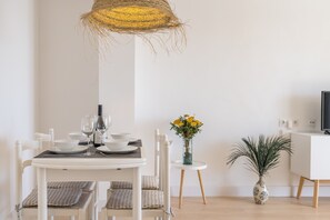 A dining area with a white table, chairs, a woven light fixture, a vase with yellow flowers, and a potted plant.