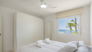 Een slaapkamer met een bed, witte handdoeken, een plafondventilator, een raam met uitzicht op zee en een deur.