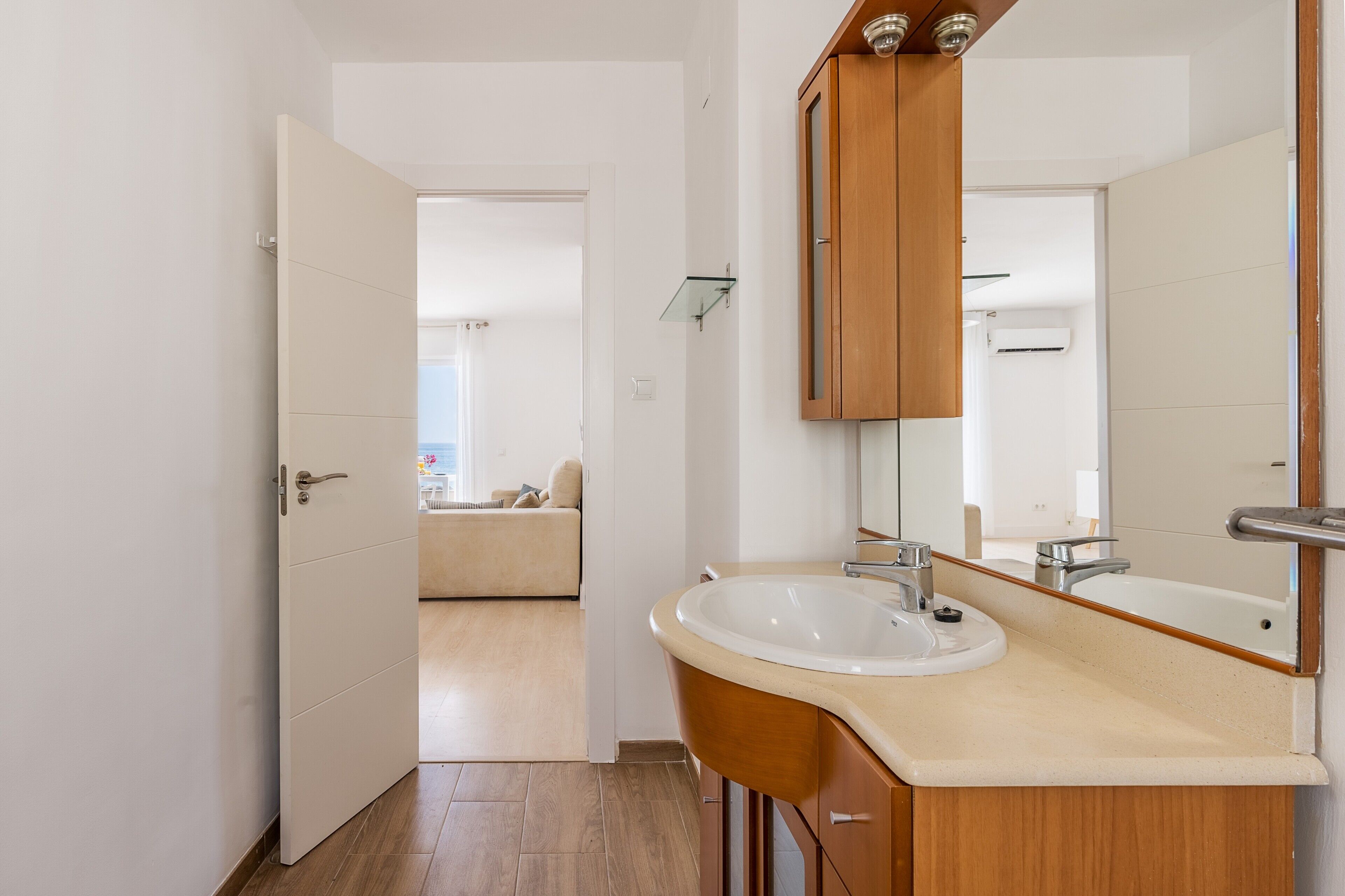 Un baño moderno con un lavamanos blanco, tocador de madera y un espejo grande.
