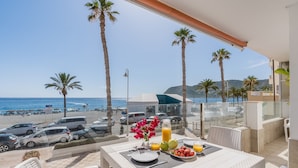 Een balkon met een ontbijttafel, met uitzicht op een strand met geparkeerde auto's en palmbomen.