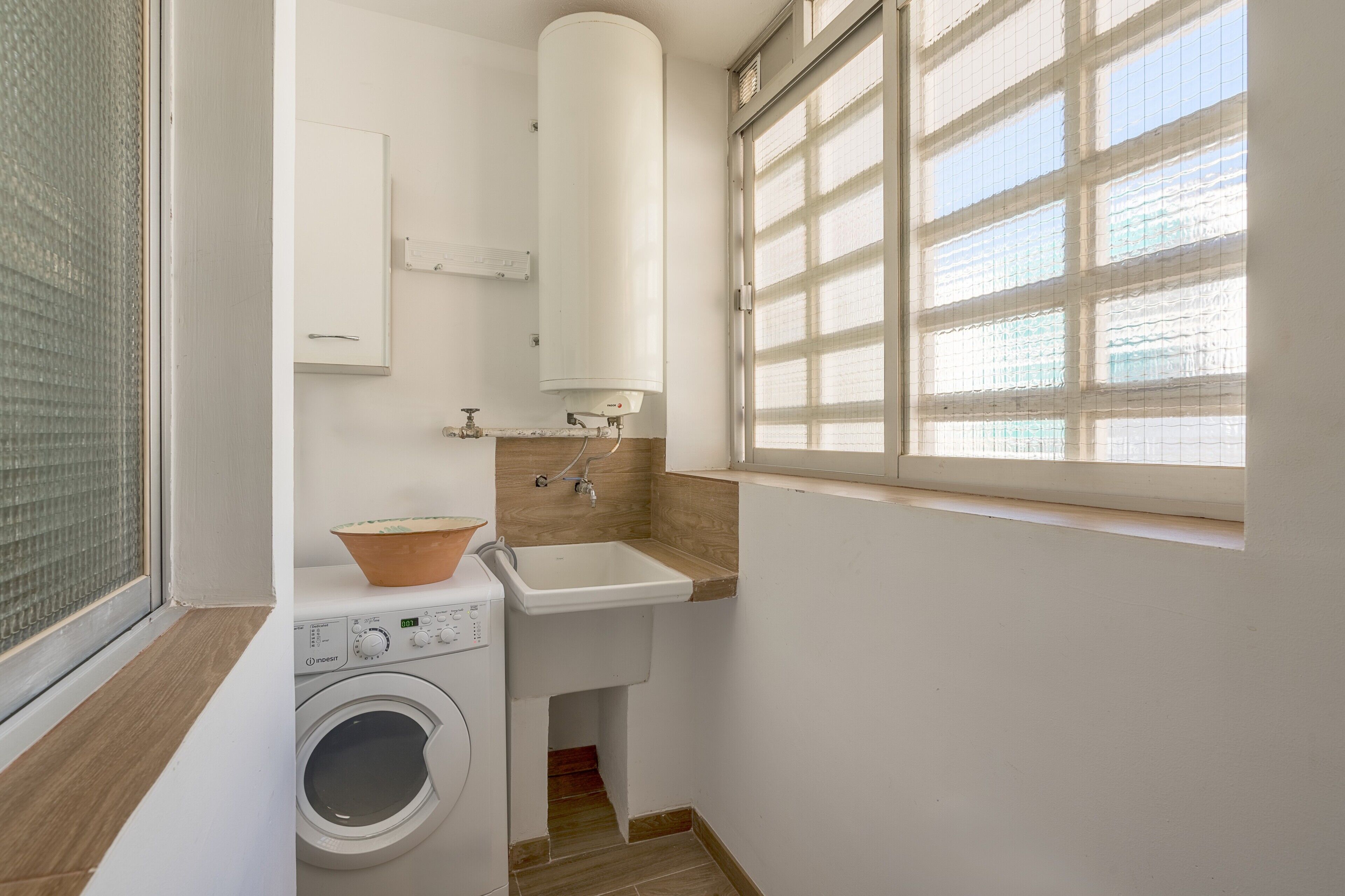 Ein kleines Badezimmer mit Waschmaschine, Waschbecken und einem Fenster mit Jalousien.