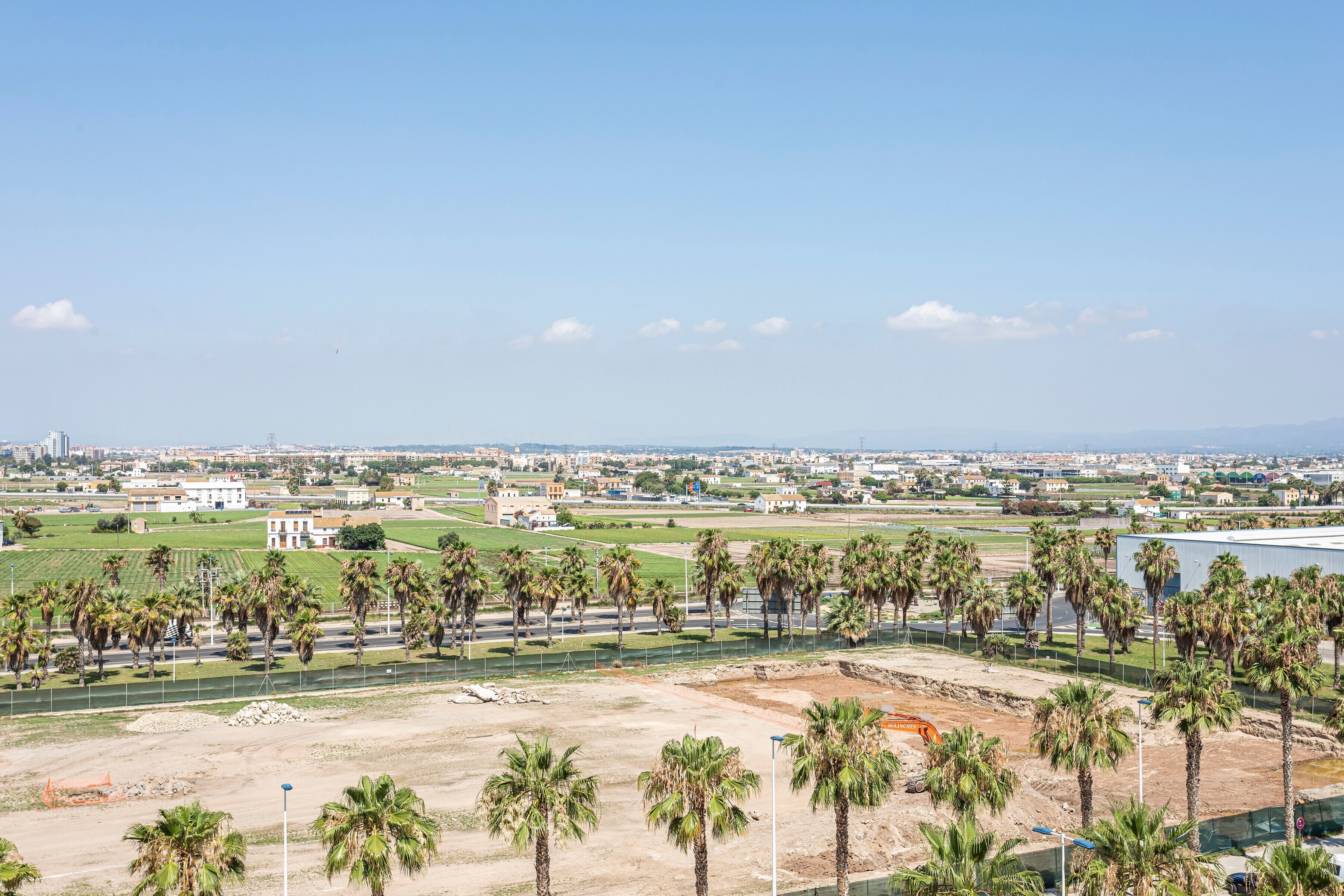 Amplia vista de un paisaje urbano costero con palmeras, un puerto deportivo y edificios industriales.