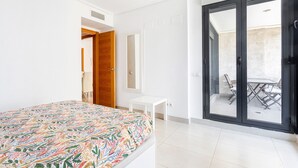 A bedroom with a bed, a small white table, a mirror, and a sliding glass door leading to an outdoor area with a table and chairs. - Apartment 'Valencia Playa' with Sea View, Wi-Fi and Air Conditioning (Alboraya)