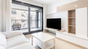 A modern living room with a sofa, a flat-screen TV, a glass coffee table, and a balcony with a view of buildings. - Apartment 'Valencia Playa' with Sea View, Wi-Fi and Air Conditioning (Alboraya)