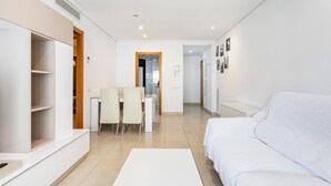 A modern living room with a white sofa, a dining area with chairs, and a kitchen visible through an open door. - Apartment 'Valencia Playa' with Sea View, Wi-Fi and Air Conditioning (Alboraya)
