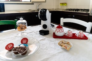 Una cocina con cafetera, un recipiente de vidrio con pasteles y una bandeja con tazas de té y galletas.