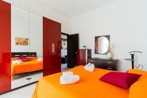 A hotel room with a bed, a wardrobe, a dresser, a mirror, and a plant.