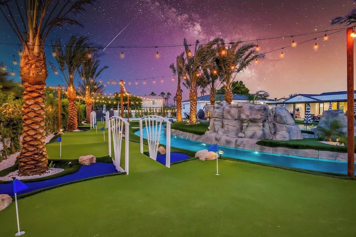 Un campo da mini golf con ostacoli d'acqua, palme e luci decorative illuminate sotto un cielo crepuscolare.