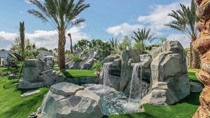 A landscaped area with rock formations, a small waterfall, and palm trees.