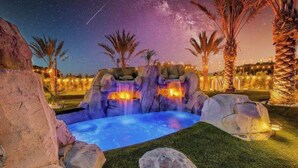 A nighttime outdoor pool area with rock formations, palm trees, and a starry sky.