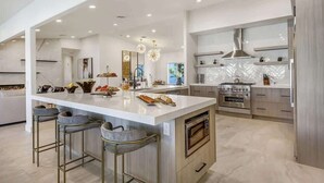A modern kitchen with a large island, bar stools, and stainless steel appliances.