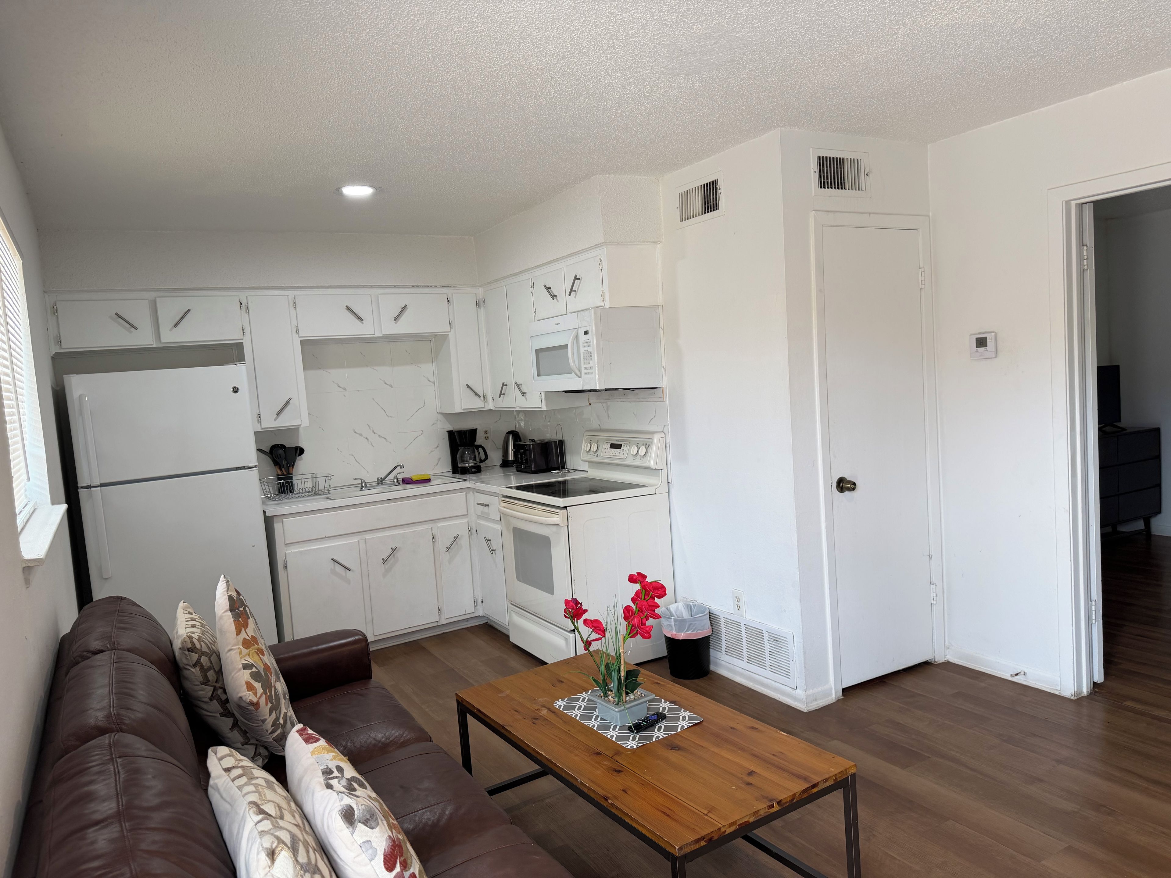 A compact kitchen with white cabinets, a refrigerator, a microwave, and a stove. There's a wooden table with a vase of flowers.