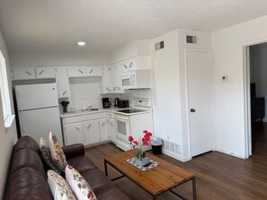 A compact kitchen with white cabinets, a refrigerator, a microwave, and a stove. There's a wooden table with a vase of flowers.