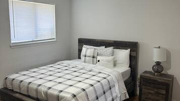 A bedroom with a bed, nightstand, and a window with blinds.