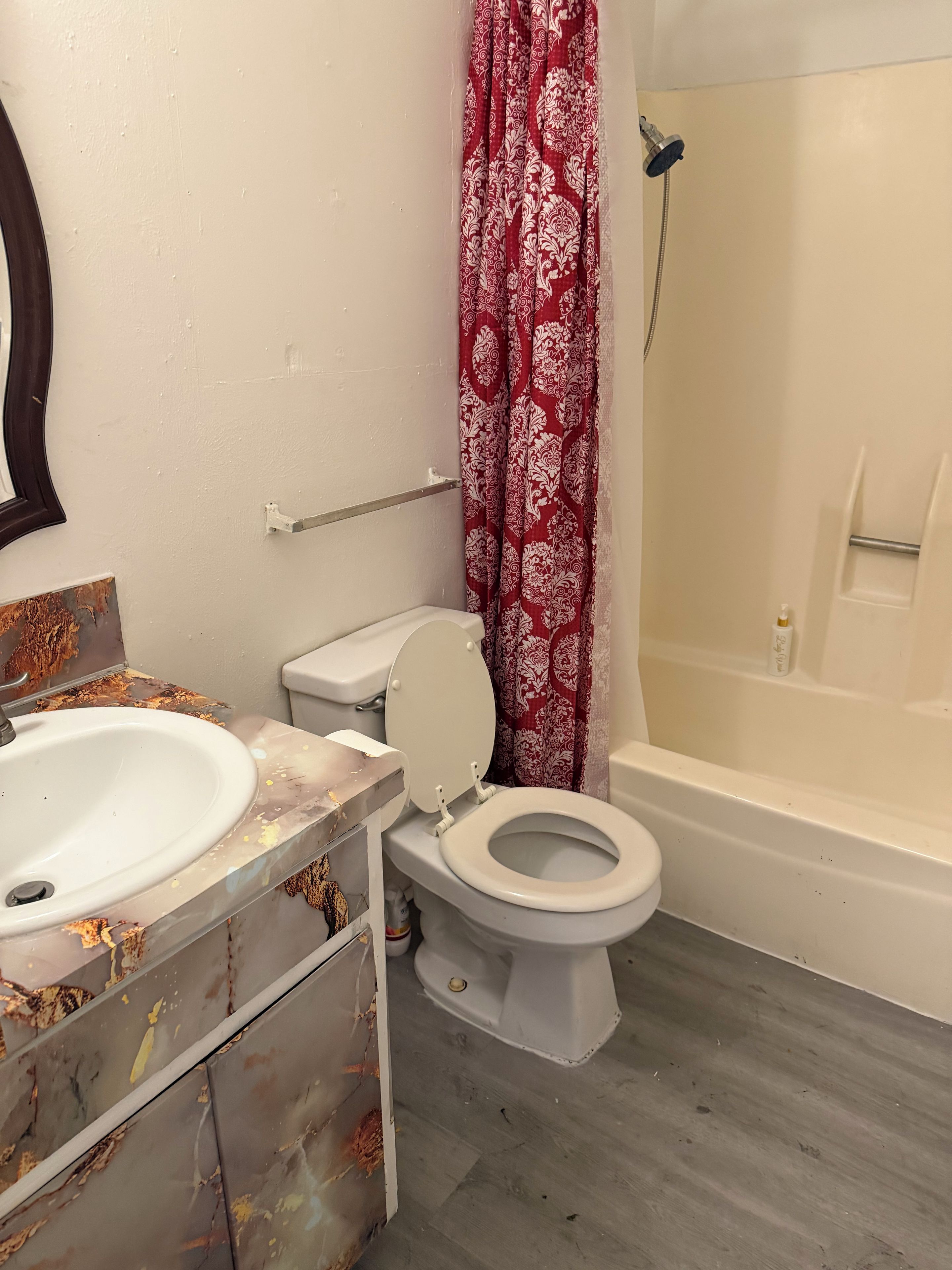 A bathroom with a toilet, sink, shower, and a mirror.