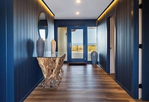 Un pasillo con suelo de madera, una isla central con un florero y una puerta que da a un balcón con vistas.