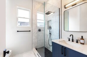 A modern bathroom with a glass-enclosed shower, a white sink with a dark faucet, and a large mirror above the sink.