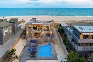 A beachfront property with a swimming pool, outdoor seating, and a view of the ocean.