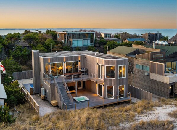 A modern house with a deck, large windows, and a view of the sea.