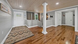 Une pièce spacieuse dotée d’un plancher en bois, d’une grande colonne blanche et d’un escalier menant à un niveau supérieur.