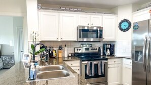 A modern kitchen with white cabinets, stainless steel appliances, and a granite countertop. - “The Disney Diamond Bungalow” (Kissimmee)