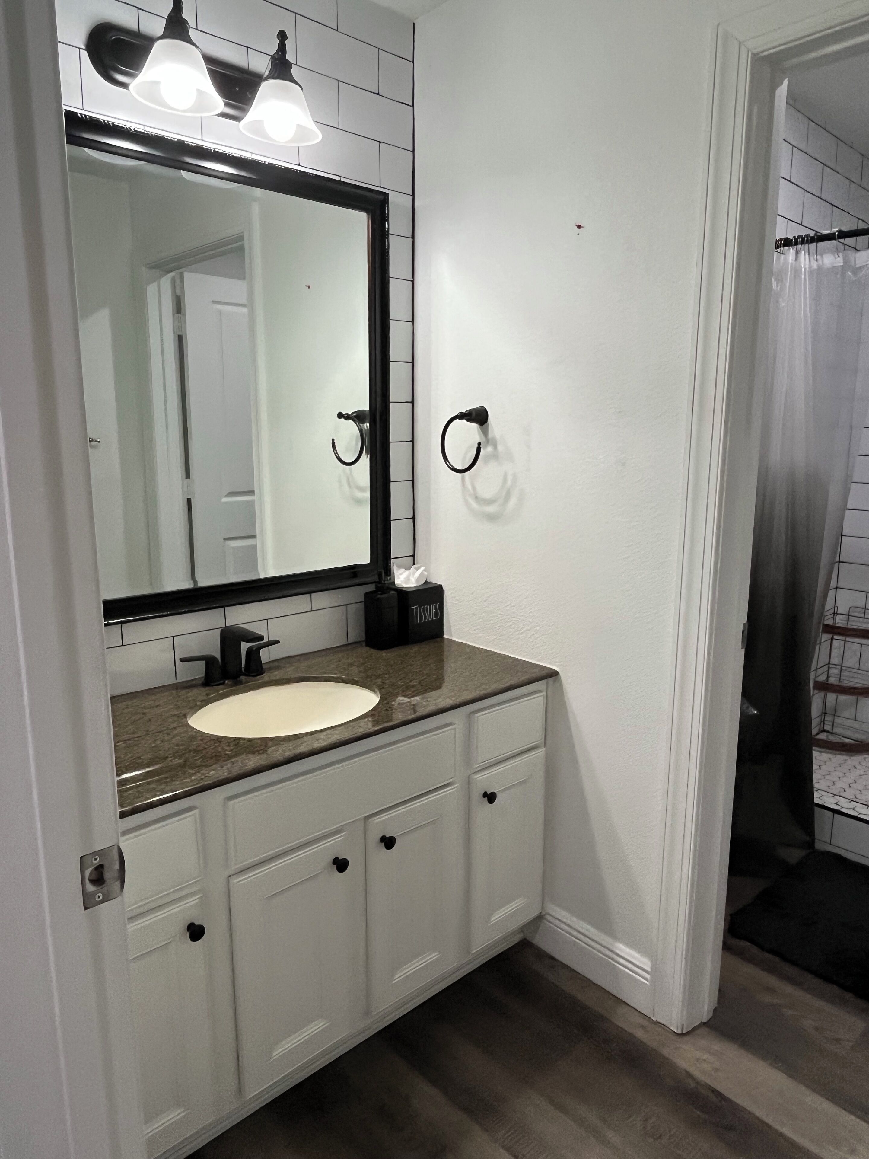 A bathroom with a white vanity, a large mirror, and a towel dispenser.