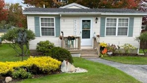 A single-story house with a front porch, a welcome sign, and a small garden with yellow flowers. - Wells Charmer 2 Bed close to Wells Beach, Restaurants, AC, WiFi. 
Sleeps 6, Deck (Wells)