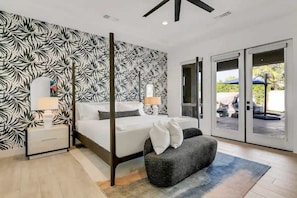 A bedroom with a bed, nightstands, a bench, a large window, and a patterned wall. - Ohana - Whale Slide, Arcade, Pickleball, Gym (Indio)