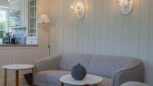 Ein Wohnzimmer mit grauem Sofa, zwei Beistelltischen und einer Lampe.