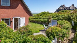 Ein rotes Backsteinhäuschen mit einem Reetdach, ein Garten mit einem Pfad und Blick auf das Meer.