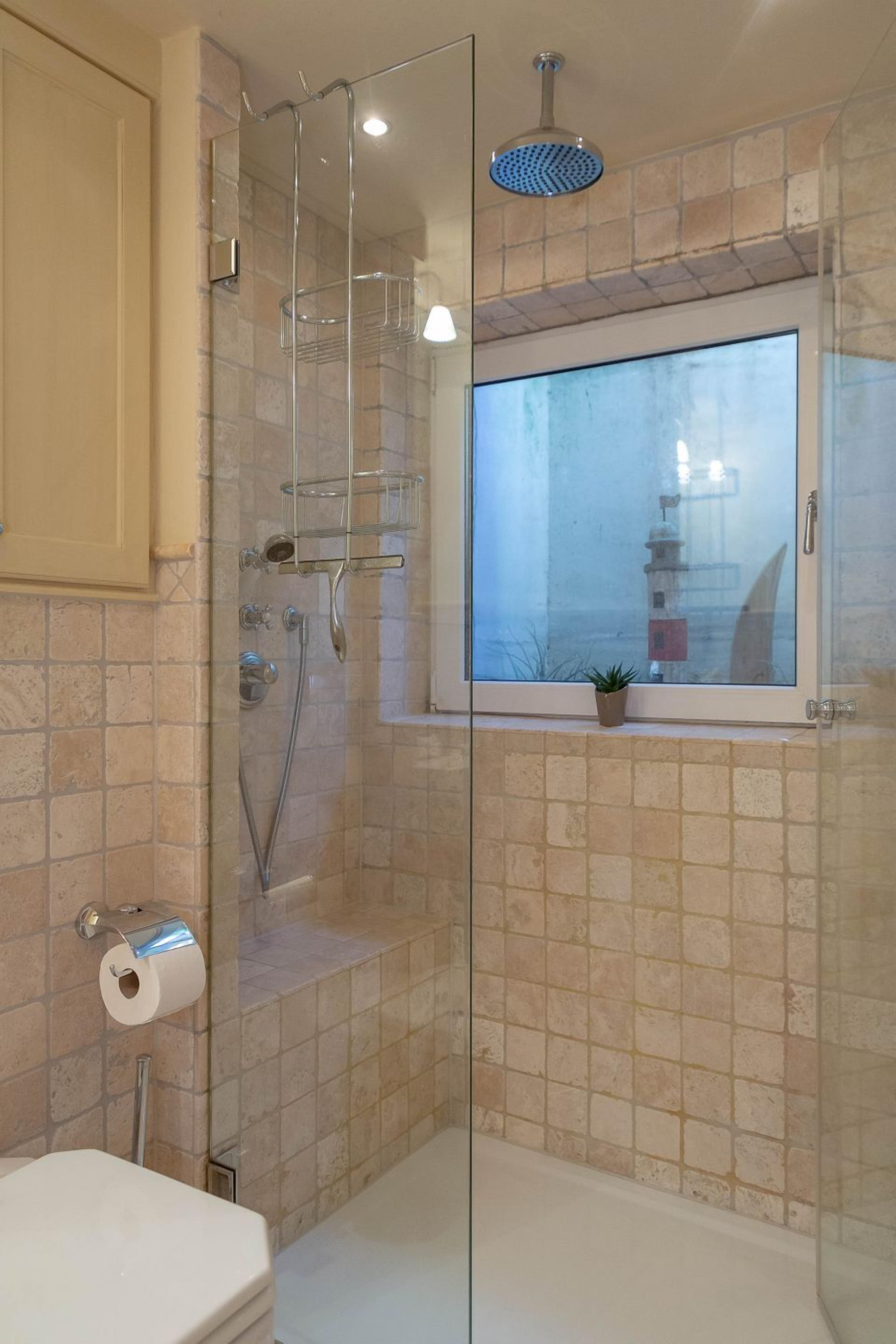 A glass-enclosed shower with a window, a toilet, and a towel rack.