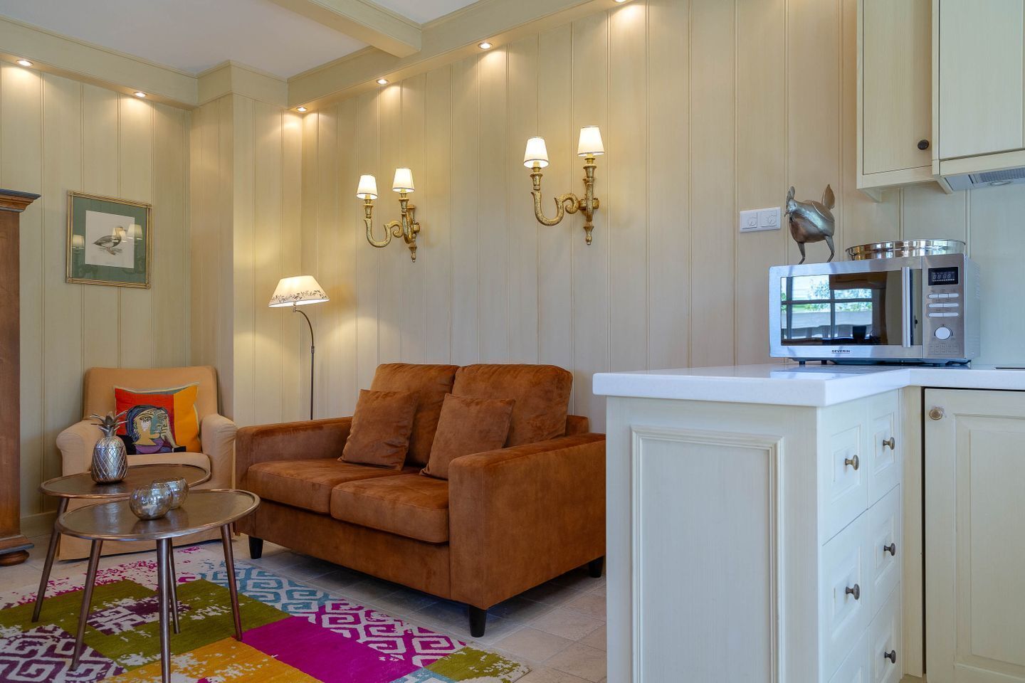A living room with a sofa, a small table, a lamp, wall sconces, a microwave, and a cabinet.
