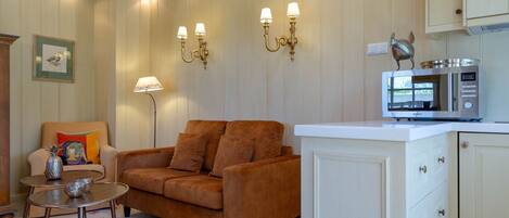 A living room with a sofa, a small table, a lamp, wall sconces, a microwave, and a cabinet.