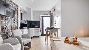 Une chambre d’hôtel moderne avec un mur d’accent en pierre, un téléviseur à écran plat, une kitchenette, un coin repas et un lit avec un plateau de petit-déjeuner.