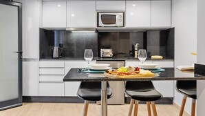 A modern kitchen with white cabinets, a black countertop, and two black bar stools. - Seaside Sunset - Fisherman s House by Homie (Calheta)