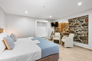 A modern bedroom with a bed, a stone wall, a TV, and a chair.