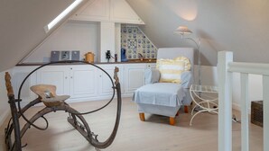 A cozy attic bedroom with a sloped ceiling, a wooden rocking chair, a small table, and a chair with a striped cushion. - Biberhüs OG - Ferienwohnung "biberhüs OG" in Archsum für bis zu 4 Personen (Archsum)