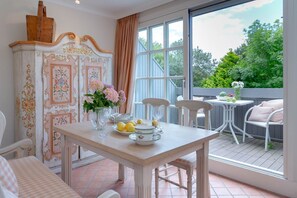 Zona pranzo con tavolo imbandito per quattro persone, un armadietto bianco con decorazioni floreali e vista sul verde attraverso ampie finestre.