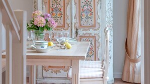 A dining area with a white table set for four, a floral cabinet, and a hanging light fixture. - Biberhüs OG - Ferienwohnung "biberhüs OG" in Archsum für bis zu 4 Personen (Archsum)