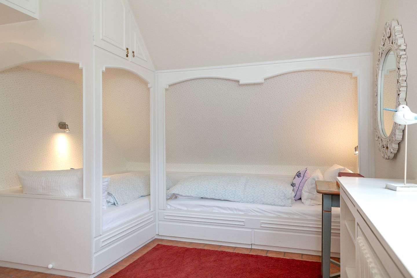 Une pièce avec un lit, un tapis rouge, un miroir et une petite table.