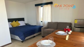 A hotel room with a bed, a sofa, a dining table with plates and a wine glass, and a refrigerator. - Single Cabin #5 - Oak Point (Ensenada)
