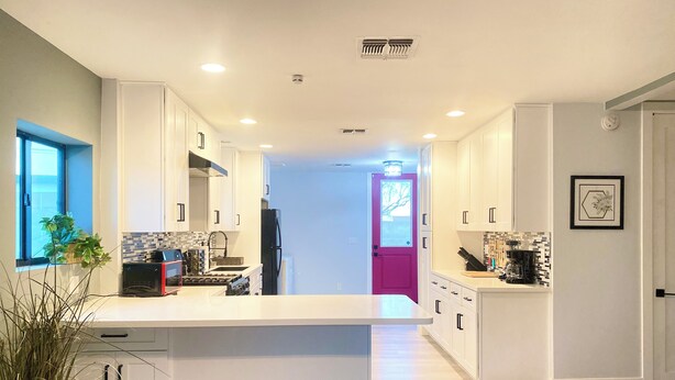 A modern kitchen with white cabinetry, a central island, and a view into the adjacent dining area.