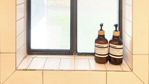 A bathroom with a window, two bottles of shampoo and conditioner, and a tiled wall.