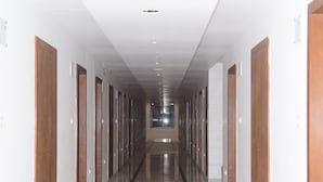 A long, narrow hallway with wooden doors on both sides and a shiny tiled floor. - The Girvar (Raipur)