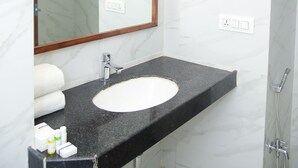 A bathroom with a marble wall, a black countertop sink, a wooden-framed mirror, and a shower. - The Girvar (Raipur)