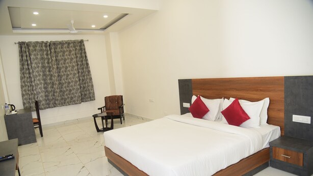 A hotel room with a large bed, a desk, a chair, and a ceiling fan. - The Girvar (Raipur)