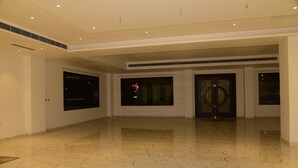 A spacious lobby with a polished marble floor, large windows, and a modern door with a circular design. - The Girvar (Raipur)